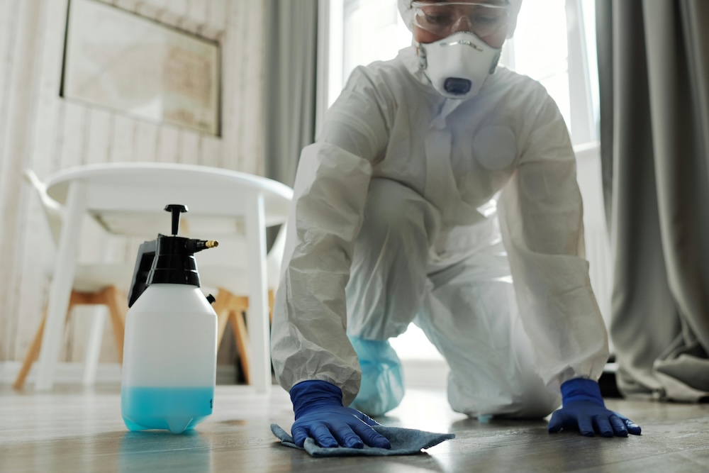 Person in protective gear sanitizing floor with disinfectant spray.